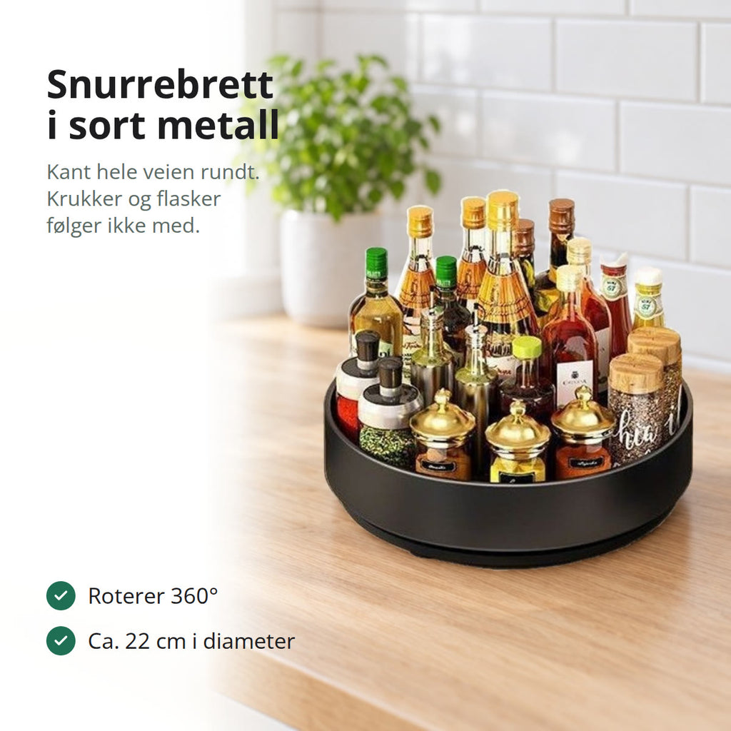 Snurrebrett i sort metall med krydderglass og olje- og eddikflasker på en lys eikebenk i et norsk kjøkken med hvite fliser