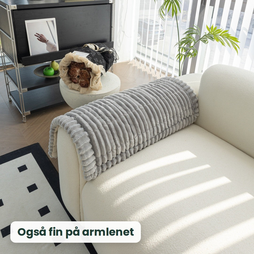 Kosla-trekk lagt over armlenet på en hvit sofa