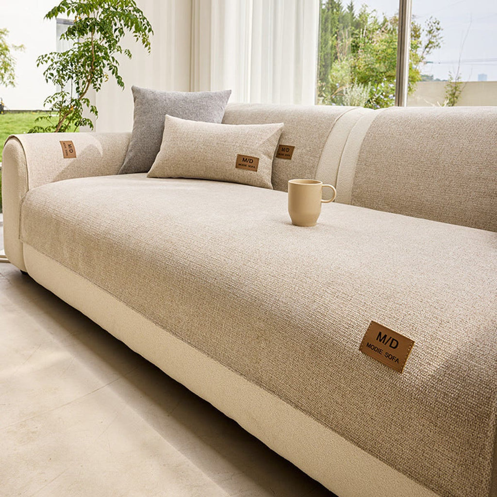 Beige sofatrekk over seteputen på en lys sofa ved et vindu