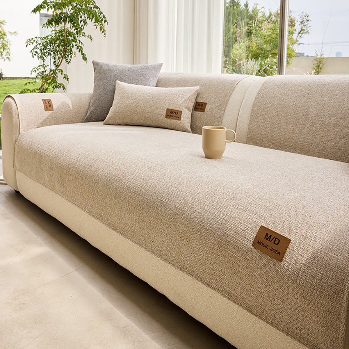 Beige sofatrekk over seteputen på en lys sofa ved et vindu