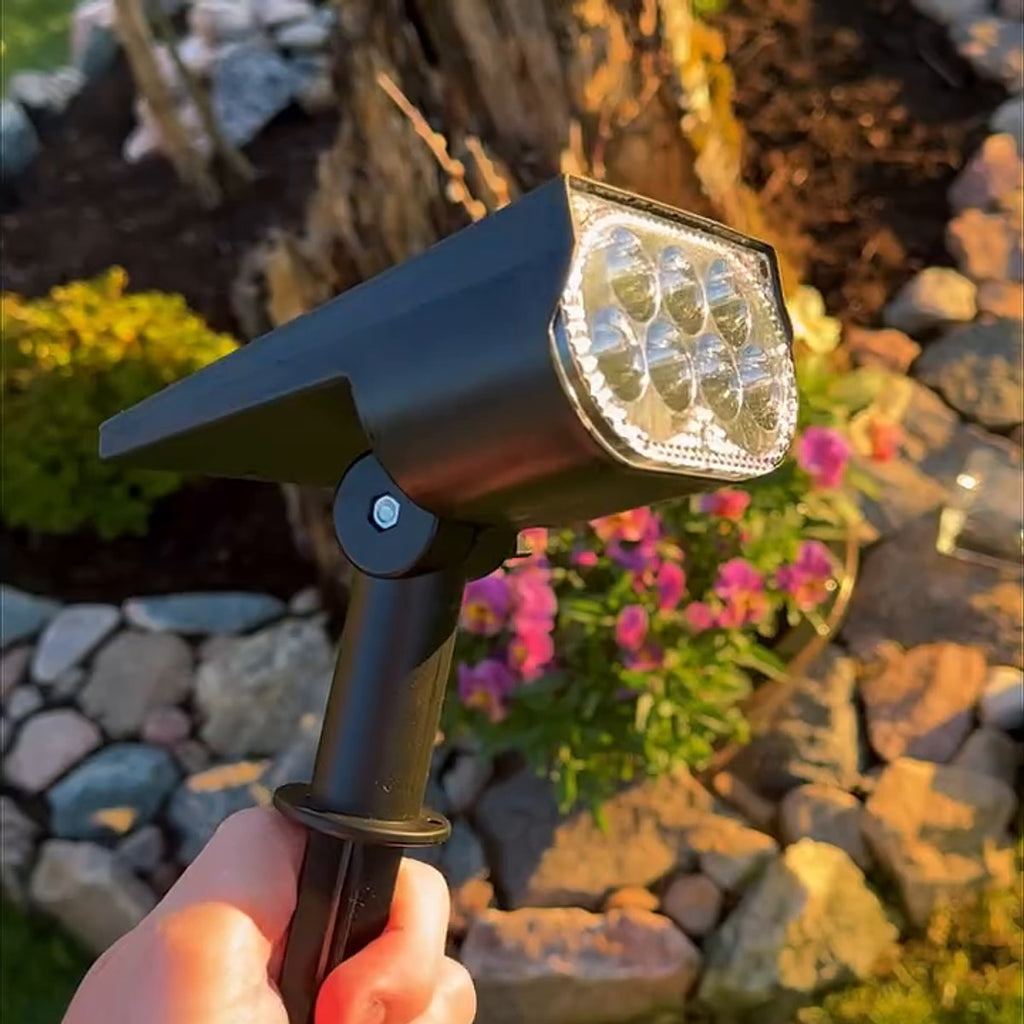 Solcelle-spotlight med 7 LED-dioder og jordspyd, holdt opp i en hage