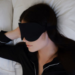 Kvinne ligger i sengen med den svarte 3D-sovemasken over øynene