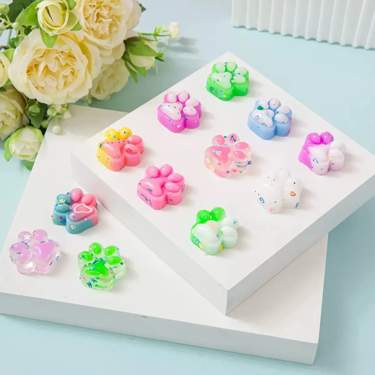 Squishy-kattepoter i pastellfarger på et hvitt podium med blomster