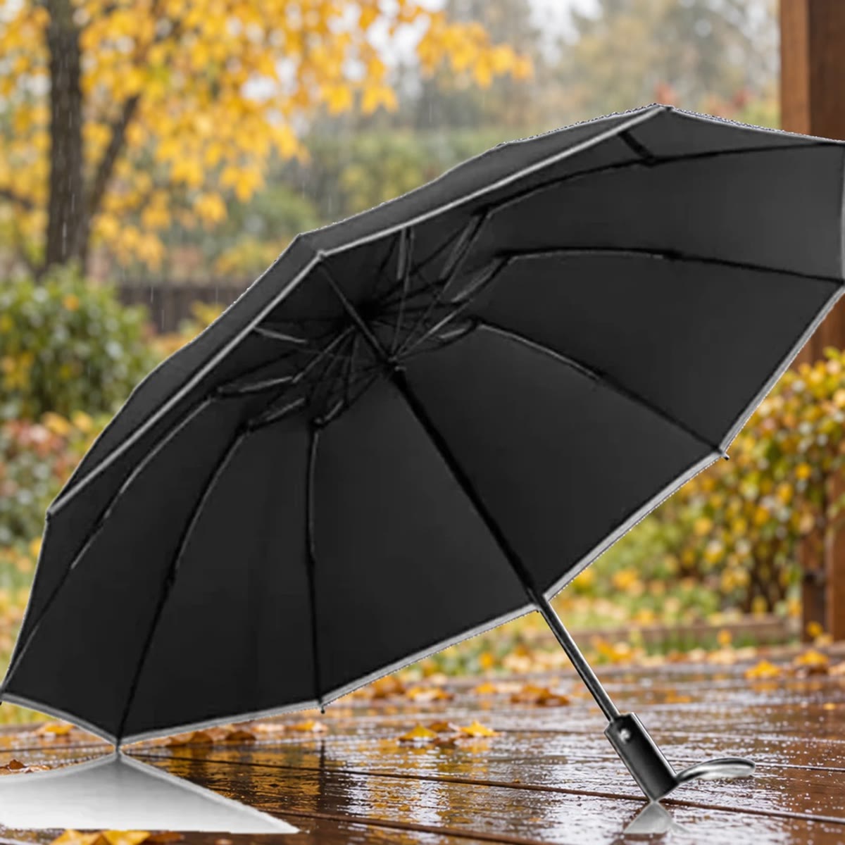 Åpen svart stormparaply med refleks langs kanten på en våt terrasse med høstløv