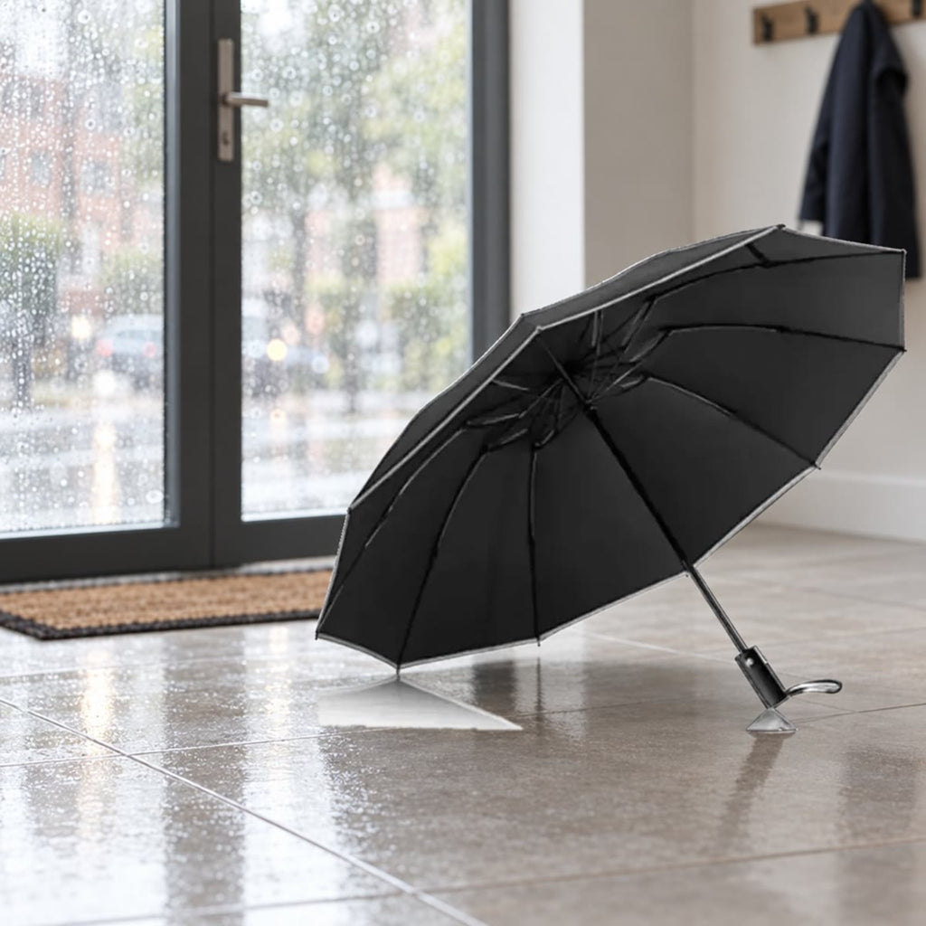 Svart stormparaply satt til tørk på flisgulvet i en gang ved en glassdør med regn