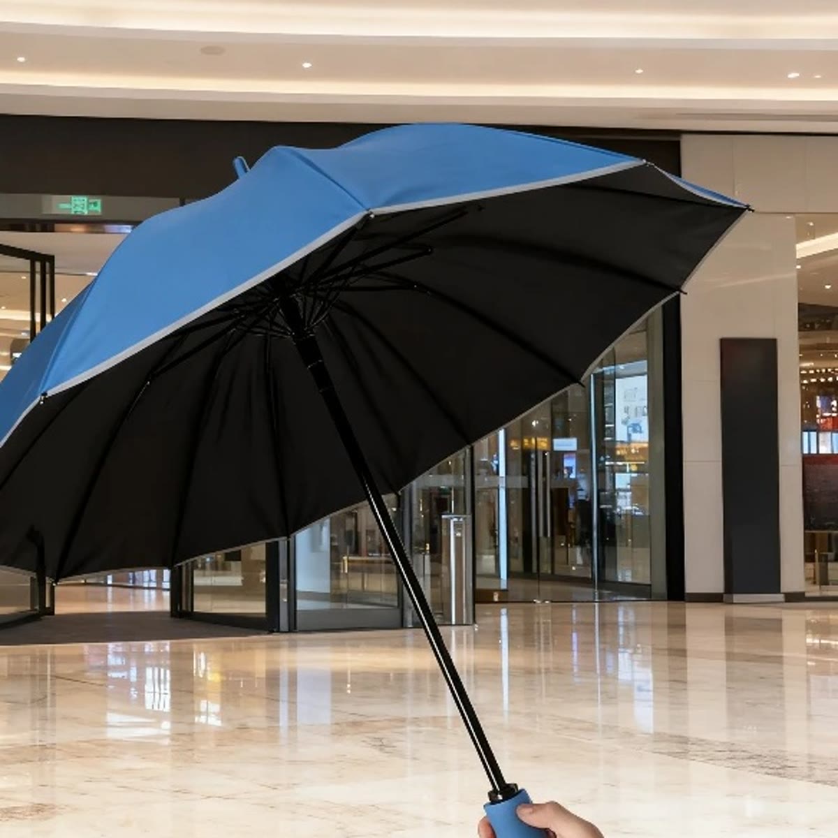 Blå stormparaply med svart underside og refleks langs kanten, holdt opp innendørs