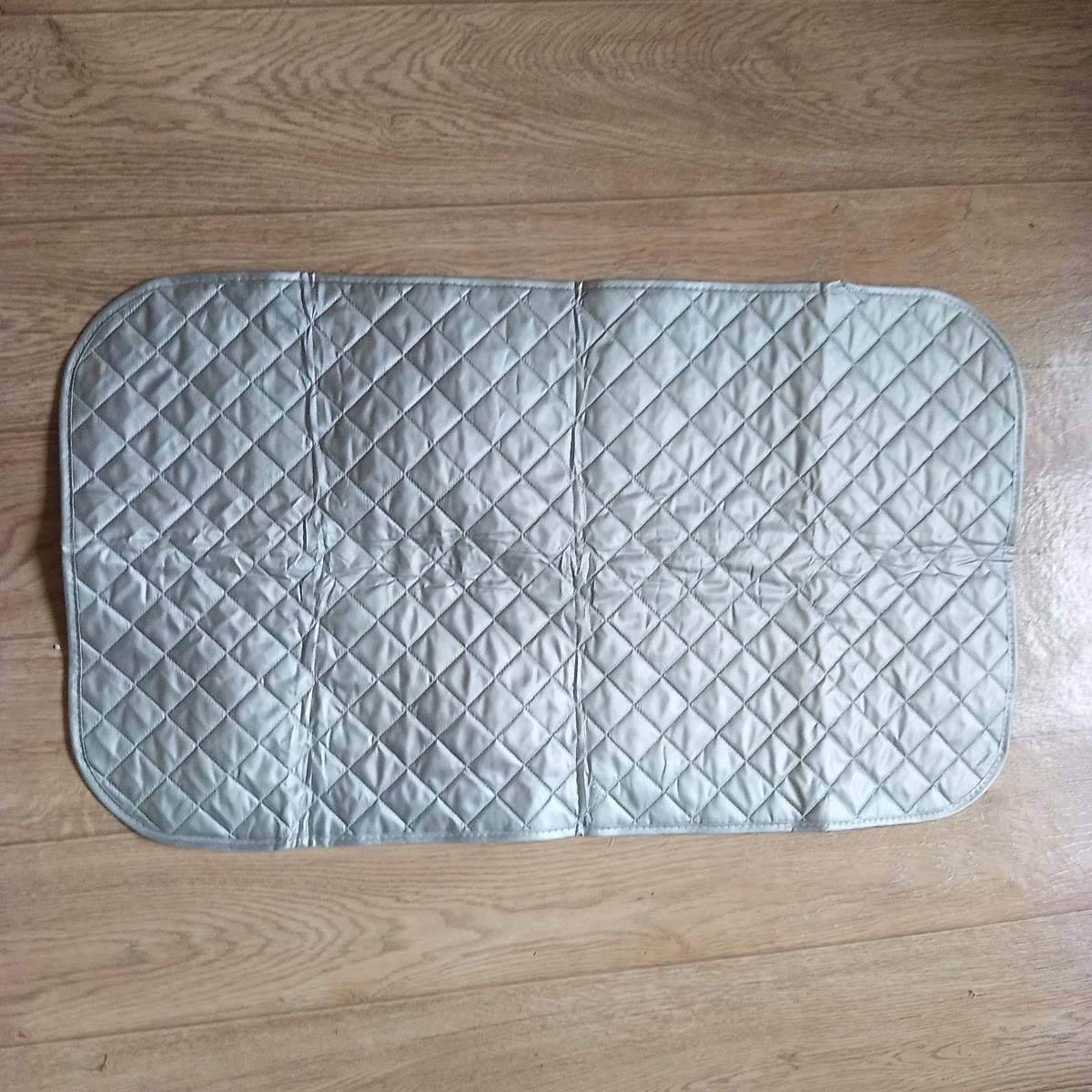 Kjøperbilde: strykematten på 48 × 85 cm lagt flatt på et tregulv, med synlige brettekanter etter frakten