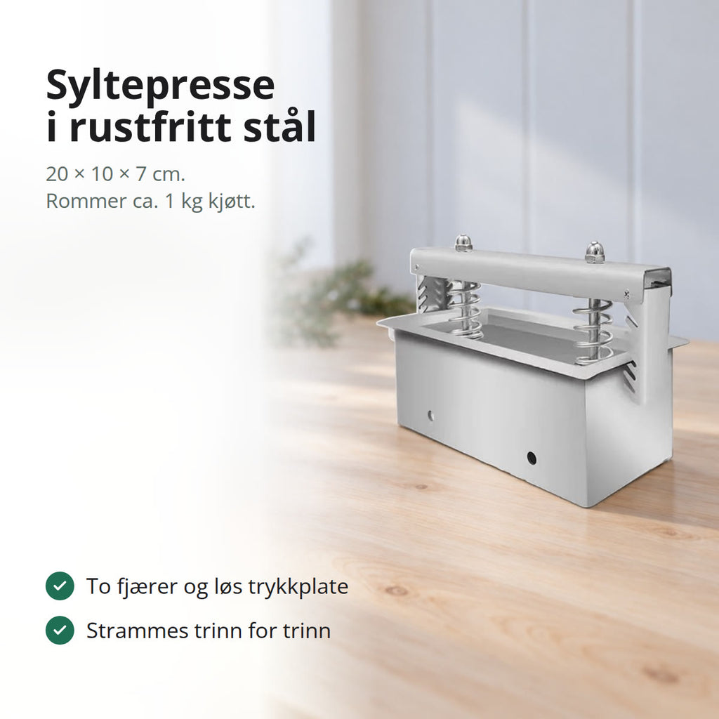 Syltepresse i rustfritt stål med to fjærer og tverrstang, stående på et lyst trebord med grankvister i bakgrunnen