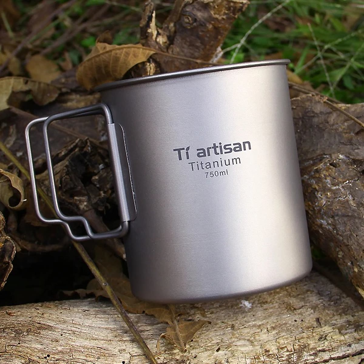 Titankjelen uten lokk, med de to håndtakene foldet ut og graveringen 750 ml, på en trestamme i skogen