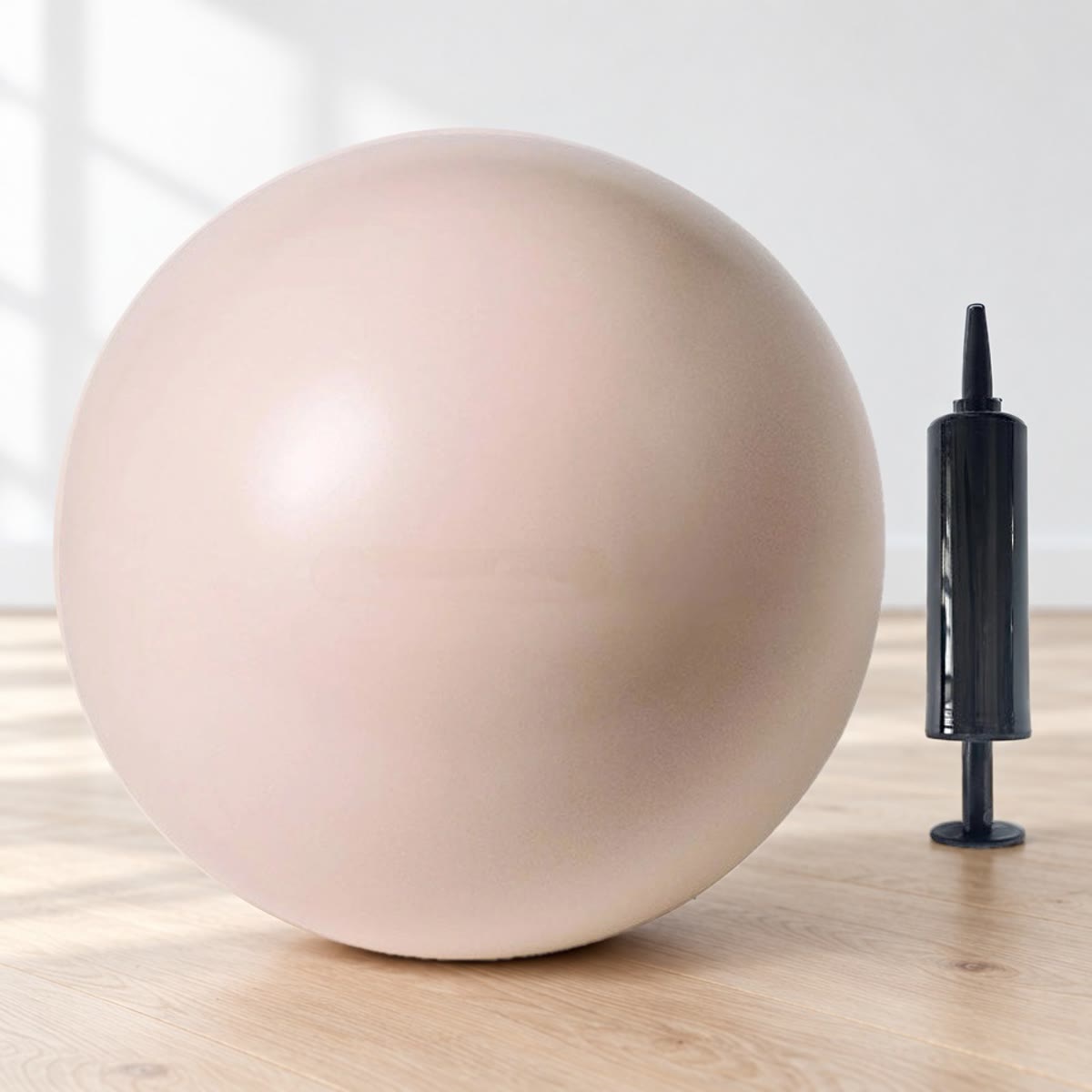 Beige pilatesball med pumpe, stående på et eikegulv mot hvit vegg