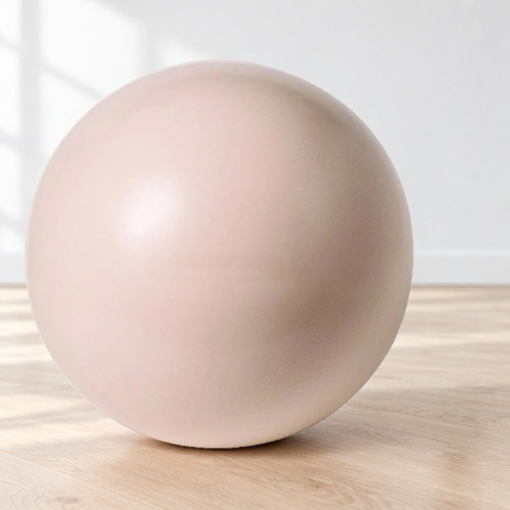 Beige pilatesball stående på et eikegulv mot hvit vegg