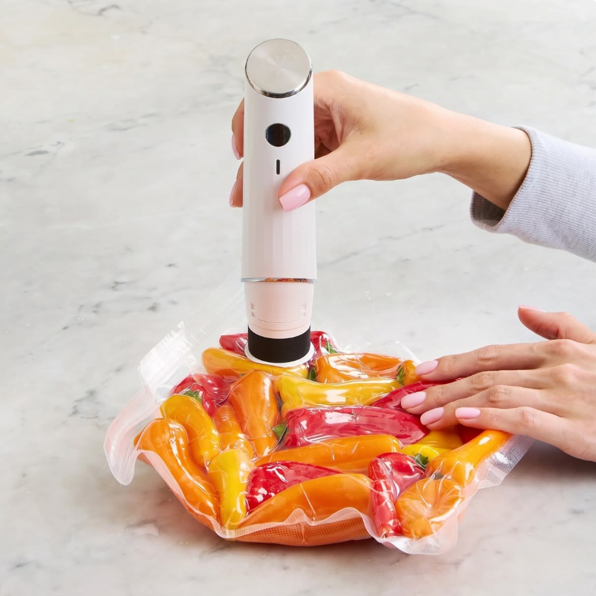 Hånd holder pumpen mot en pose med røde og gule paprika på en benk