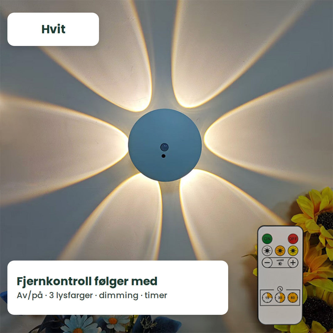 Hvit Lysblom-lampe på veggen med et blomstermønster av lys rundt seg og fjernkontrollen ved siden av