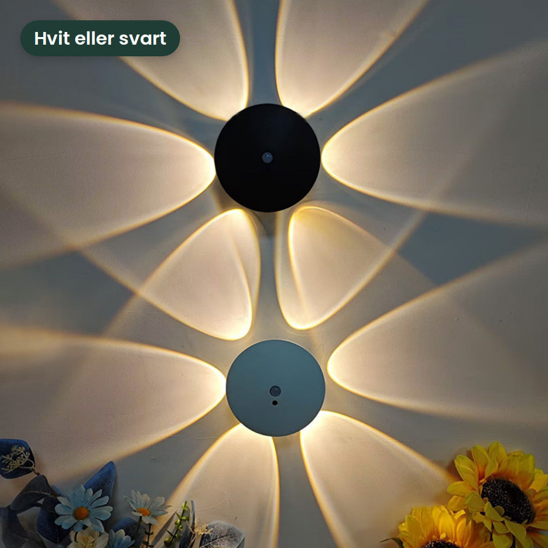 En hvit og en svart lampe på samme vegg med hvert sitt blomstermønster av lys
