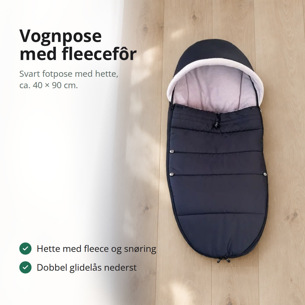 Svart vognpose med lyst fleecefôr og hette, liggende flatt på et lyst eikegulv ved et vindu