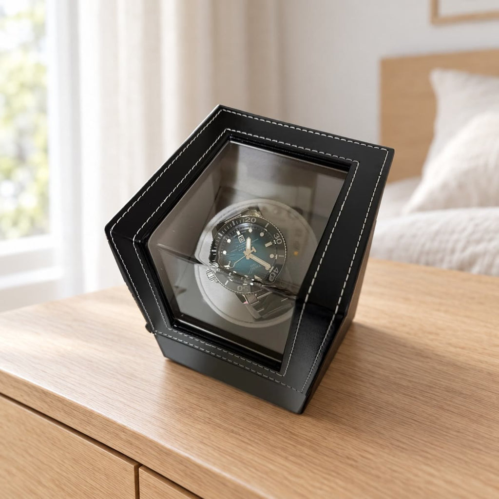 Watch winder i svart kunstskinn med hvite sømmer og en klokke bak vinduet, på en kommode i lys eik i et soverom