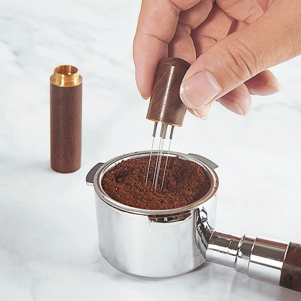 Hånd som rører med WDT-verktøyet i kaffepulveret i en filterkurv, med lokket ved siden av