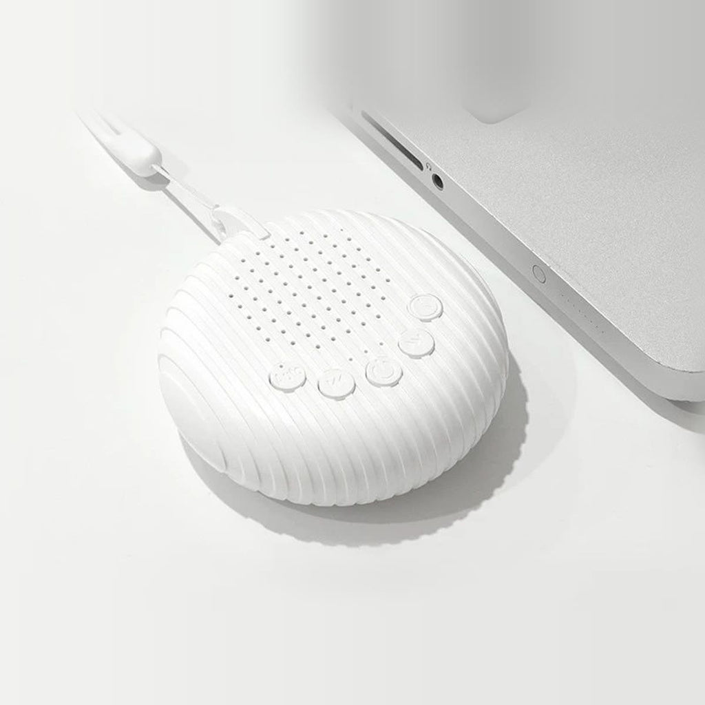 Rund white noise maskin sett ovenfra på en hvit pult ved siden av en laptop