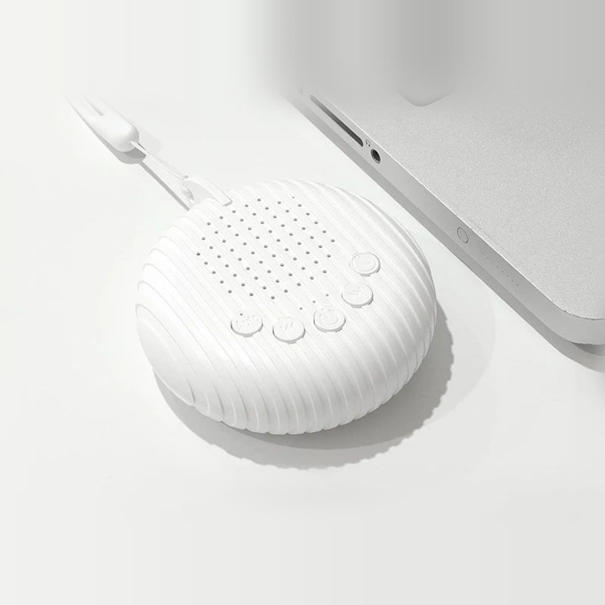 Rund white noise maskin sett ovenfra på en hvit pult ved siden av en laptop