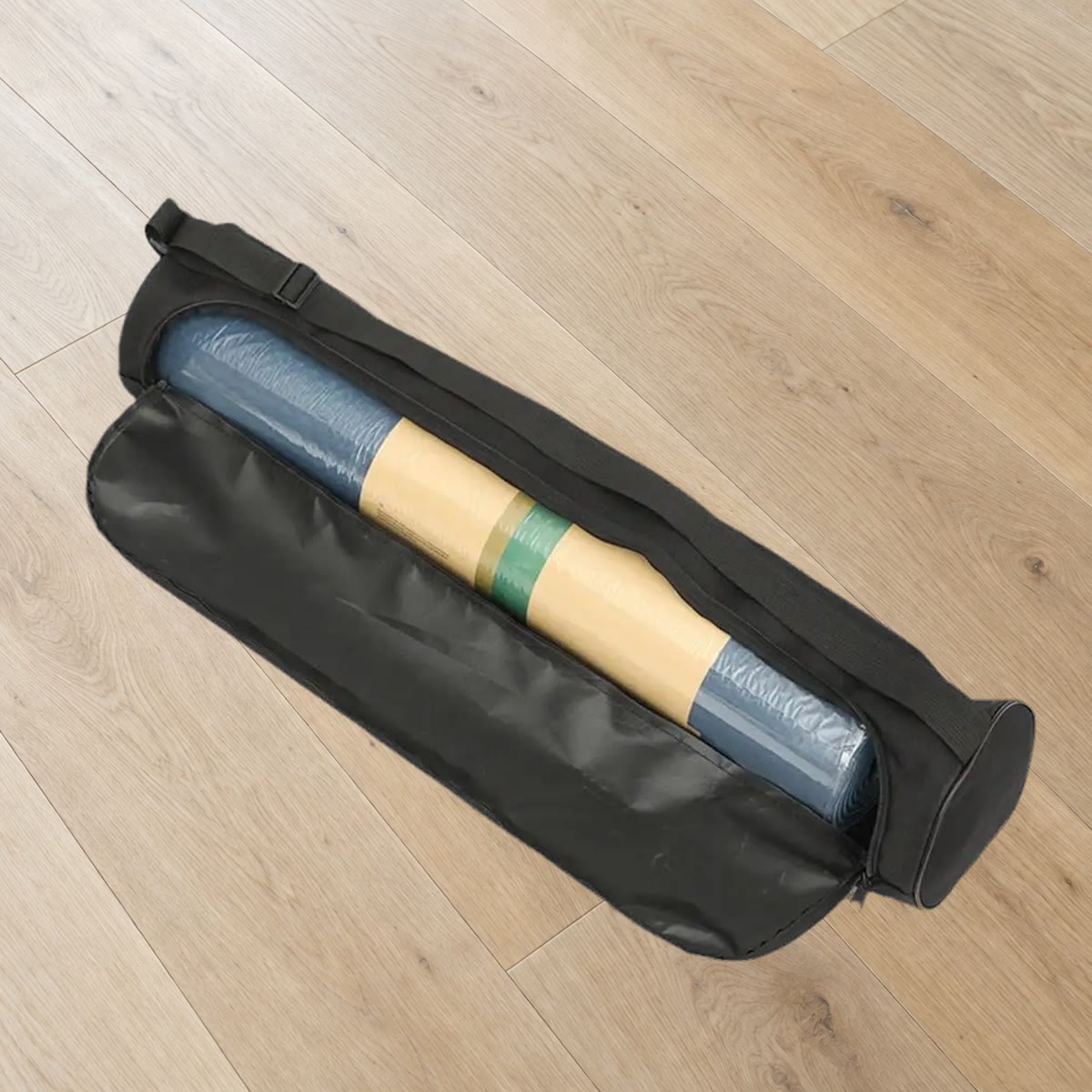 Svart yogamatte bag åpnet langs siden med en rullet yogamatte inni, på et eikegulv (matten følger ikke med)